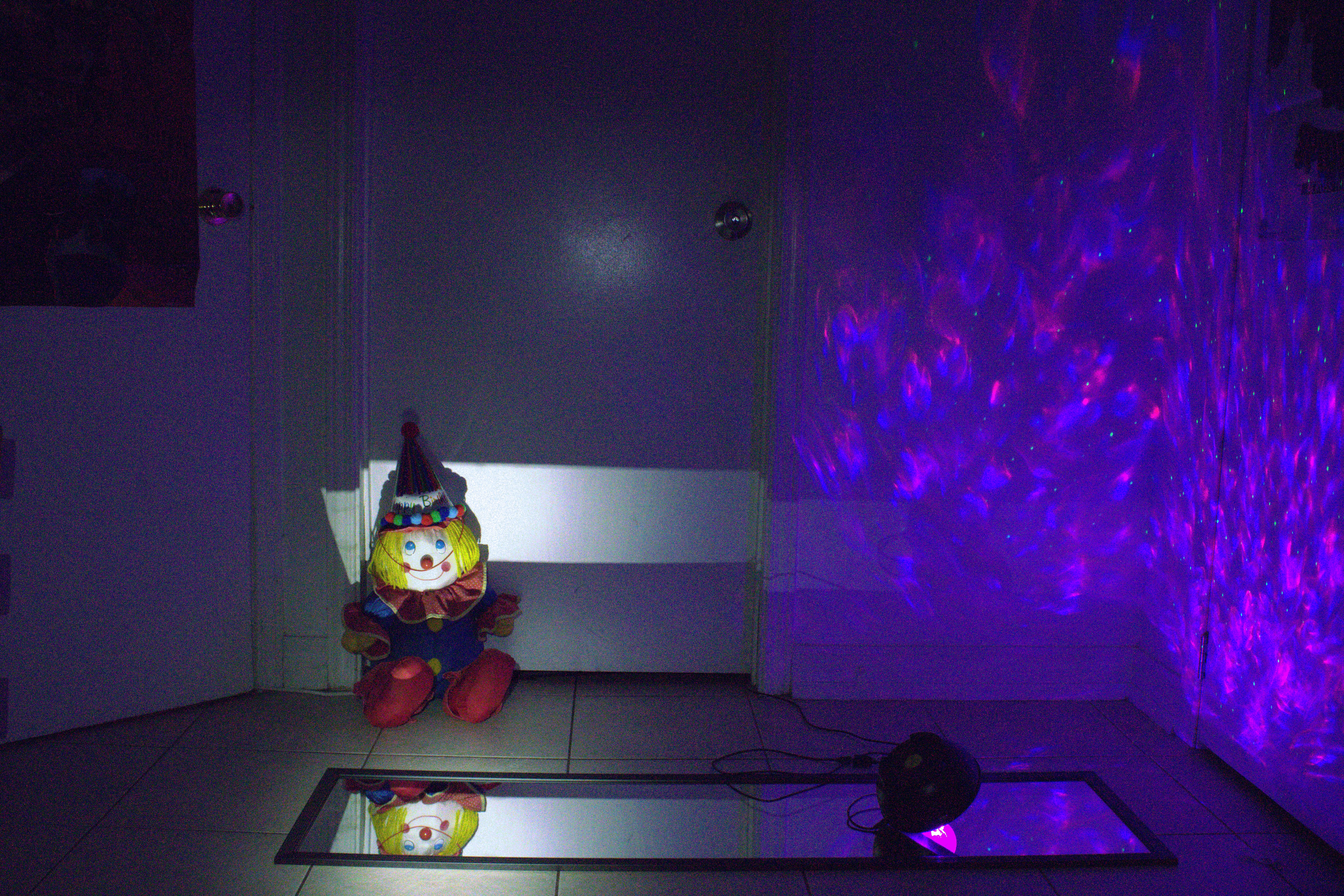 A clown doll wearing a birthday hat sits infront of a closed door
